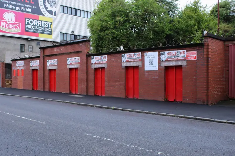 Row of red turnstile doors set into a brick wall outside a football ground