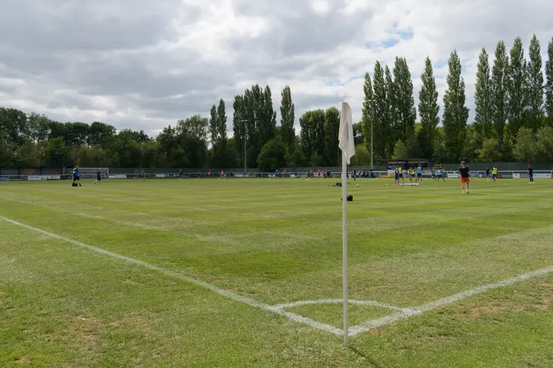 A non-league football match seen from beside the corner flag on a cloudy day