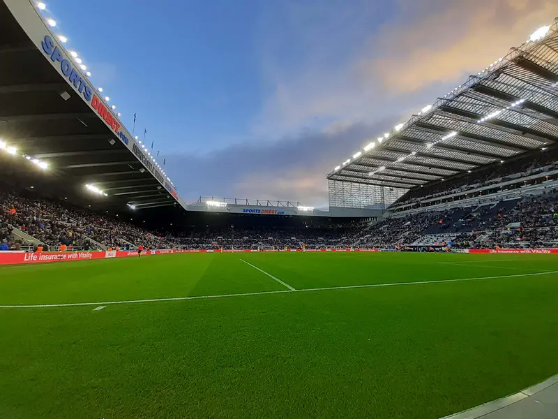 St James' Park football ground under floodlights at dusk, seen from pitch level